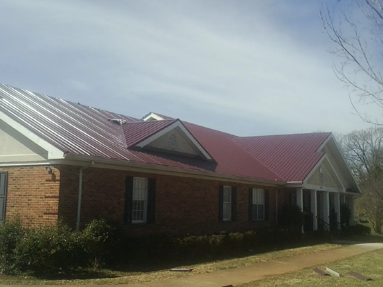 Red metal roof with gabled entries on a long brick building, from a Hail Damage Roof Repair job in Lawrenceburg